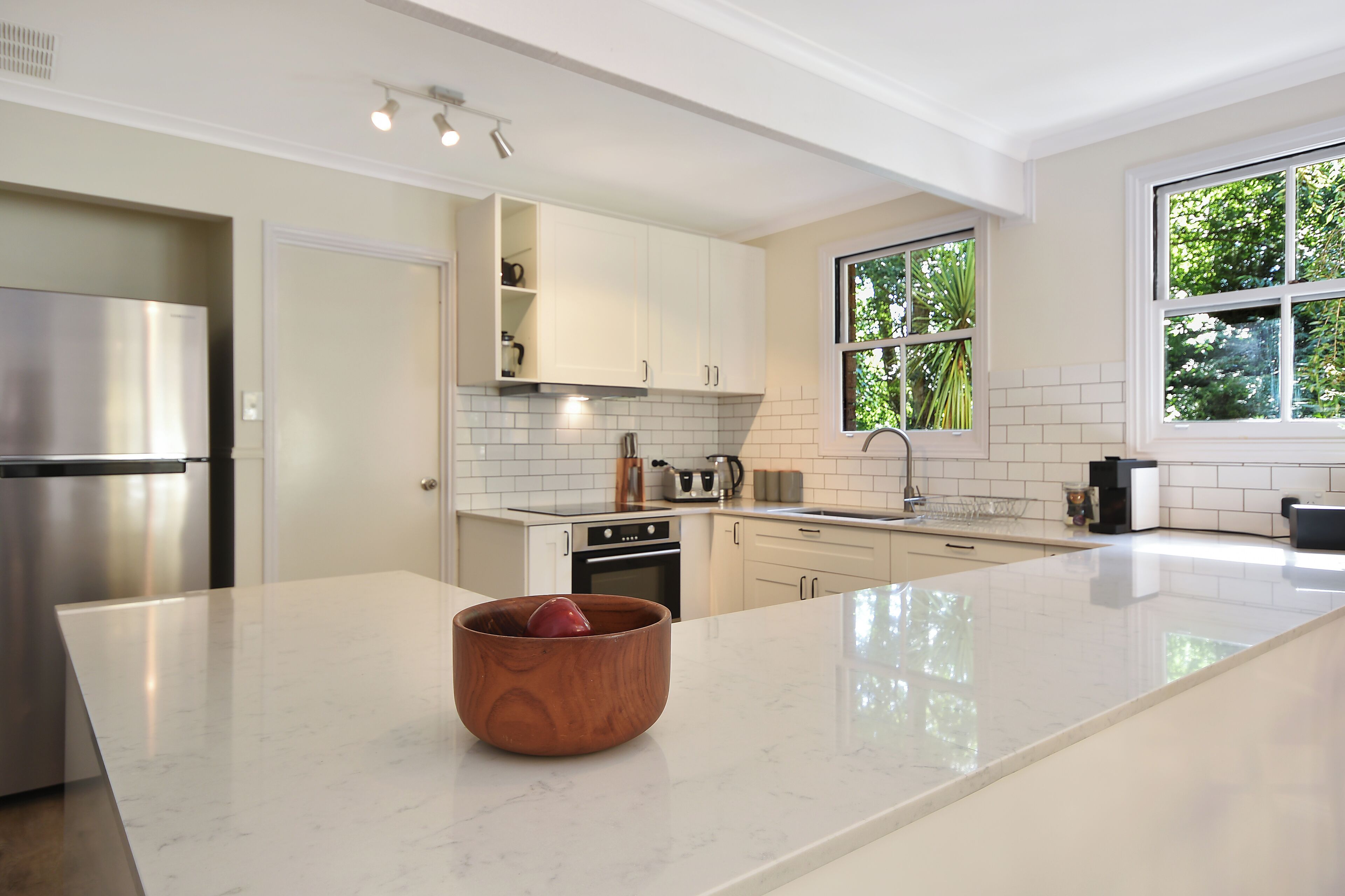 A modern kitchen with white cabinetry, a stainless steel refrigerator, and a wooden bowl on the island.