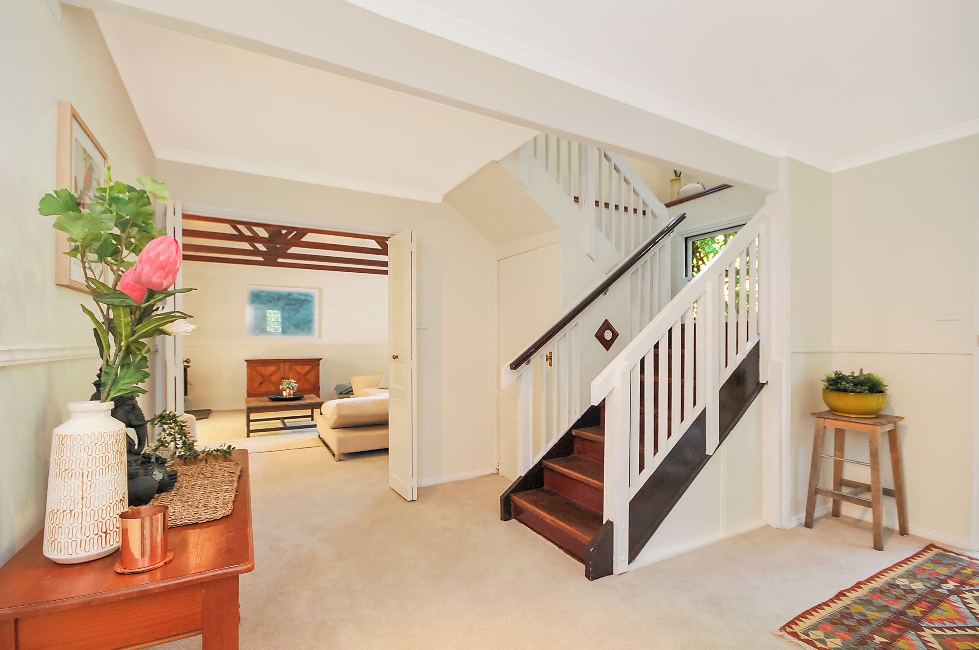 A staircase with wooden steps and white railings, leading to a room with a beige carpet and a colorful rug.