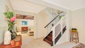 A staircase with wooden steps and white railings, leading to a room with a beige carpet and a colorful rug.