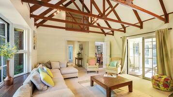 A spacious living room with a high ceiling, a sofa set, a coffee table, and a view through a glass door.