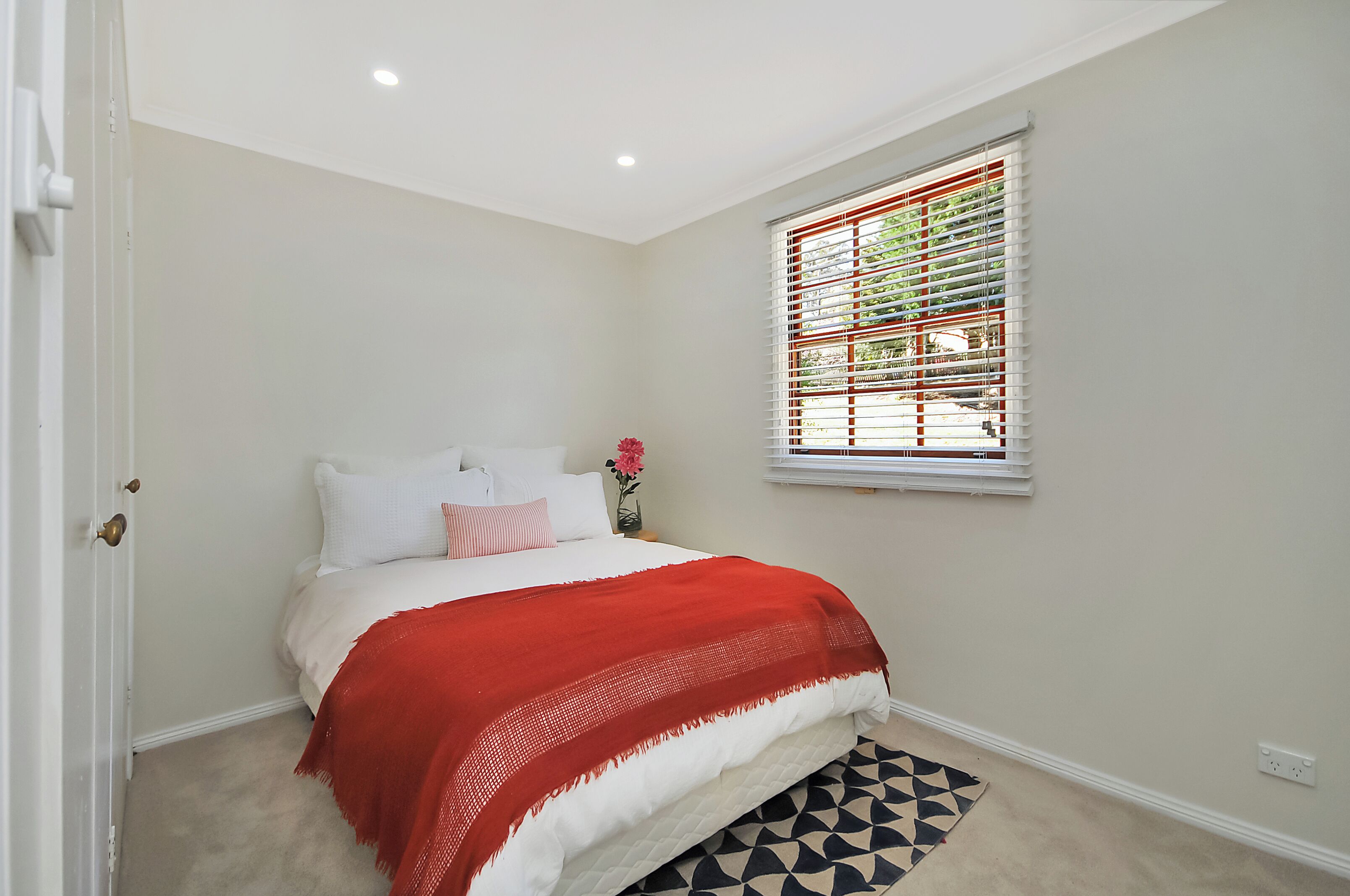 A bedroom with a bed, a window with blinds, a door, and a patterned rug.
