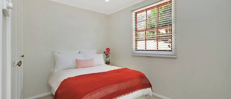A bedroom with a bed, a window with blinds, a door, and a patterned rug.
