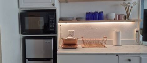 Una cucina con forno a microonde, frigorifero, una pentola sul piano di lavoro e scaffali con utensili da cucina.