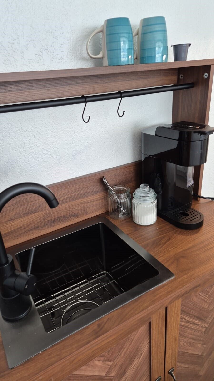 A kitchen with a black sink, a coffee maker, and a spice rack.