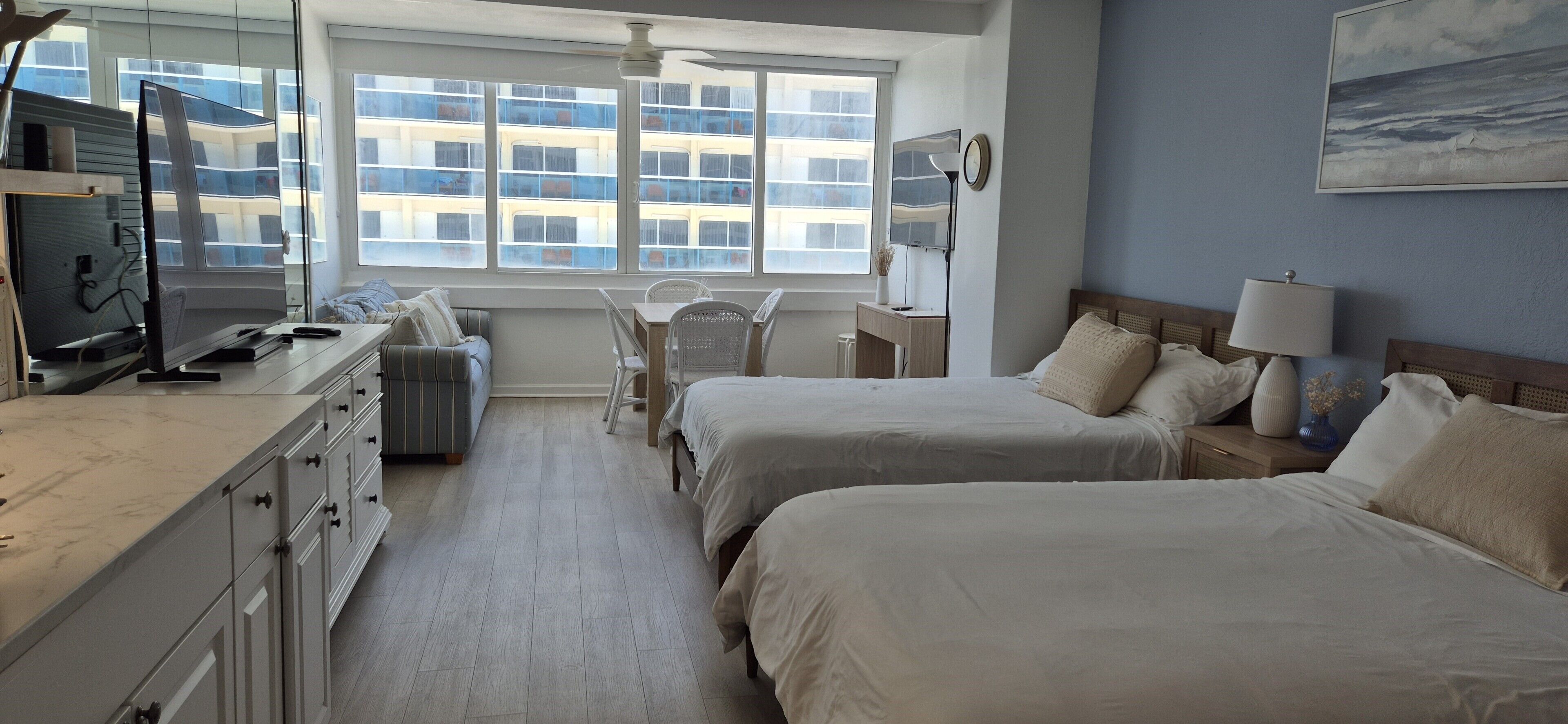 Une chambre d’hôtel avec deux lits, un bureau, une chaise, une télévision et une fenêtre donnant sur des immeubles.
