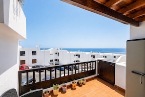 A balcony with a view of the sea, white buildings, and parked cars.