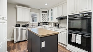 Una cocina moderna con armarios blancos, una isla central, electrodomésticos de acero inoxidable y un horno negro.