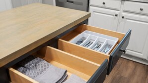 Una cocina con armarios de madera, una encimera y un cajón con utensilios y toallas dobladas.