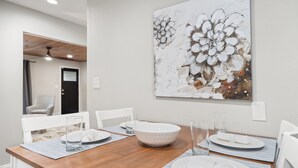 Un comedor con una mesa de madera dispuesta para cuatro, sillas blancas y un cuadro grande con motivos florales en la pared.