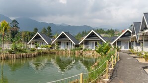 A row of bungalow-style cabins with a pond in the foreground, surrounded by lush greenery and mountains in the background. - Salma Syariah by TwoSpaces, Bogor (Cisarua)