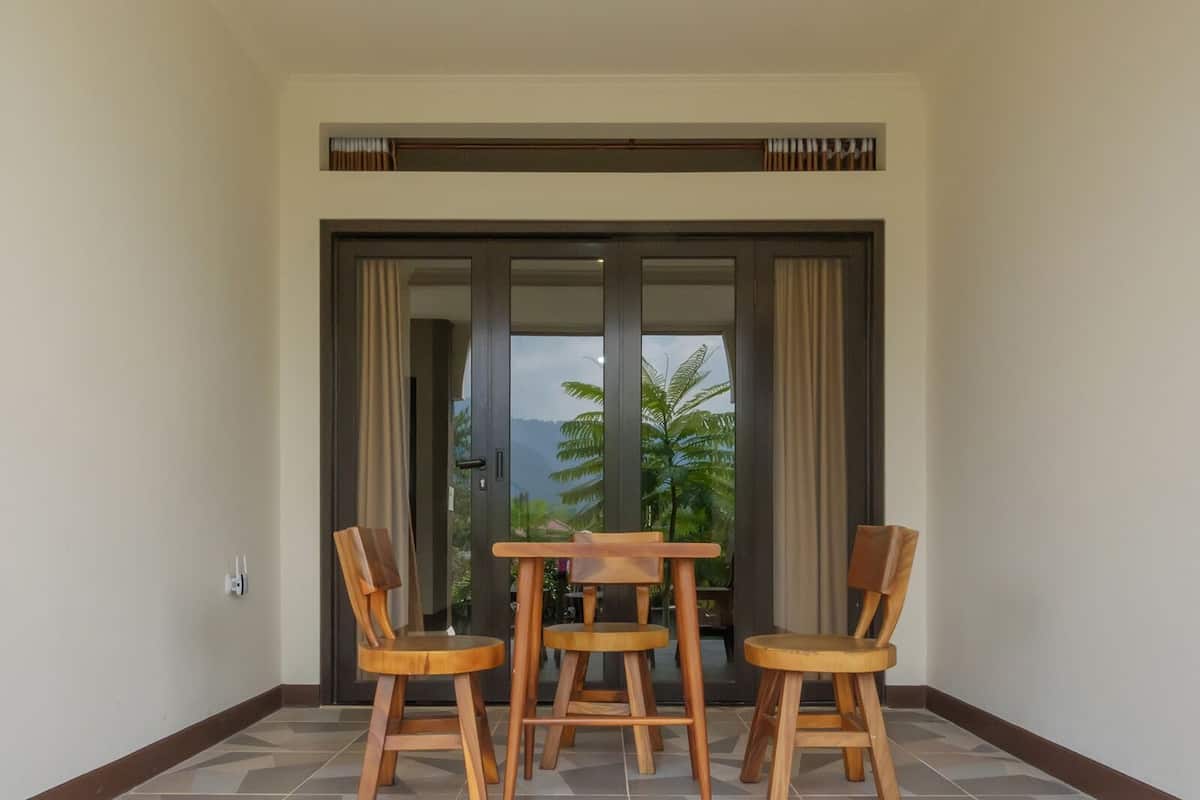 Quarto com porta de vidro deslizante para uma varanda, mesa de madeira com quatro cadeiras e chão ladrilhado.