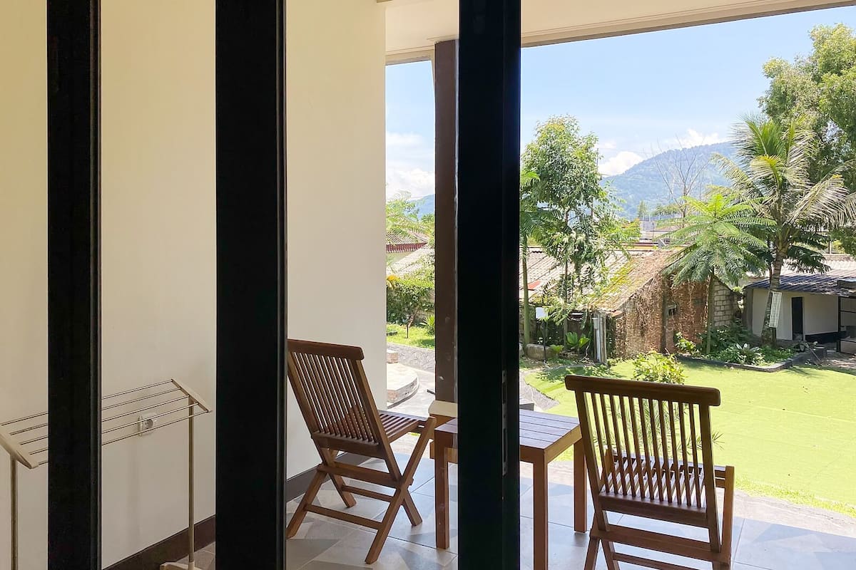 Varanda com duas cadeiras de madeira e uma mesa, com vista para um jardim bem cuidado e montanhas distantes.