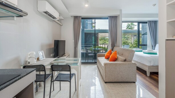 A modern hotel room with a kitchenette, a sofa with orange cushions, a bed, and a balcony with a view of greenery. - Surin Beachside Sun Escape C209 (Choeng Thale)