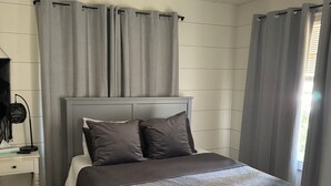 Un dormitorio con cama, mesita de noche, ventilador de techo y cortinas.