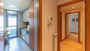 A modern kitchen with built-in cabinets, a refrigerator, and a stove. There is a wooden door leading to another room, and a wall-mounted phone. - GuestReady - Serenity home in Porto (Boavista)