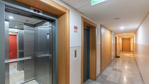 A hotel corridor with an elevator, wooden doors, and a fire exit sign. - GuestReady - Serenity home in Porto (Boavista)