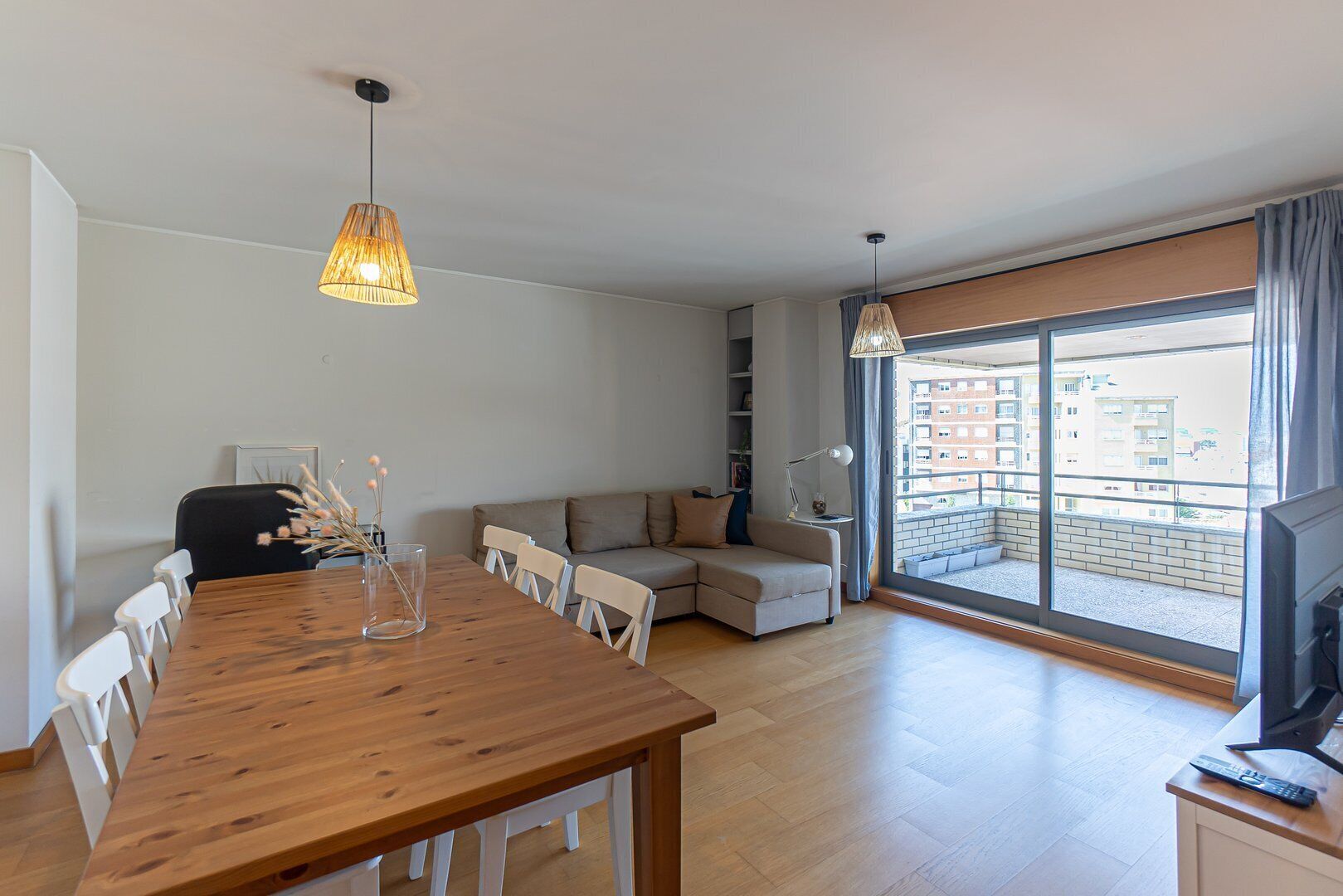 A modern apartment with a dining area, a sofa, a TV, and a balcony with a city view.