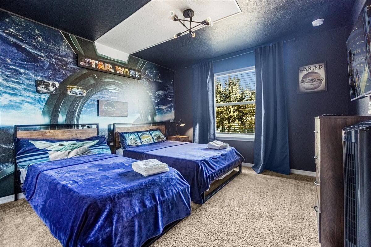 A room with two beds, a large window with curtains, a Star Wars themed wall, and a 'WANTED' poster.
