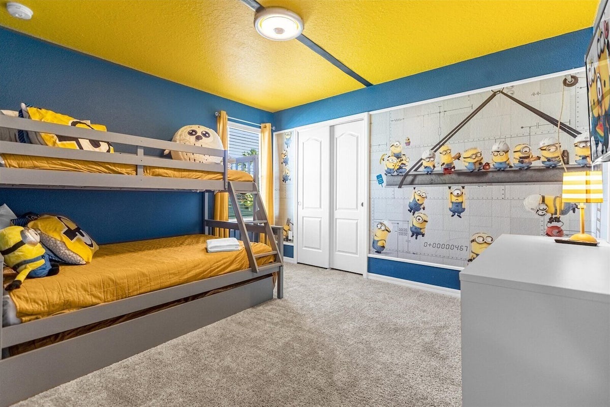 A bunk bed room with a Minion-themed wall and a desk with a lamp.