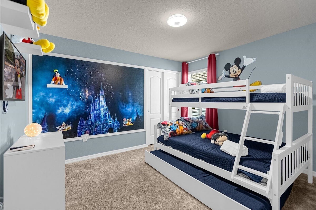 A child's bedroom with a bunk bed, a Disney-themed wall mural, and a desk with a plush toy.