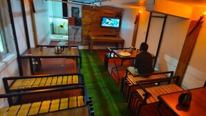 Ein gemütliches Restaurant mit Holztischen und -stühlen, einem Fernseher im Hintergrund und einem grünen Teppich.
