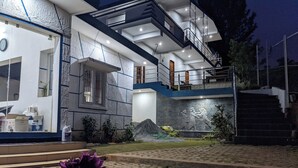Ein modernes, zweistöckiges Haus mit Naturstein-Fassade, einem Balkon und einem angelegten Garten mit einem befestigten Weg.