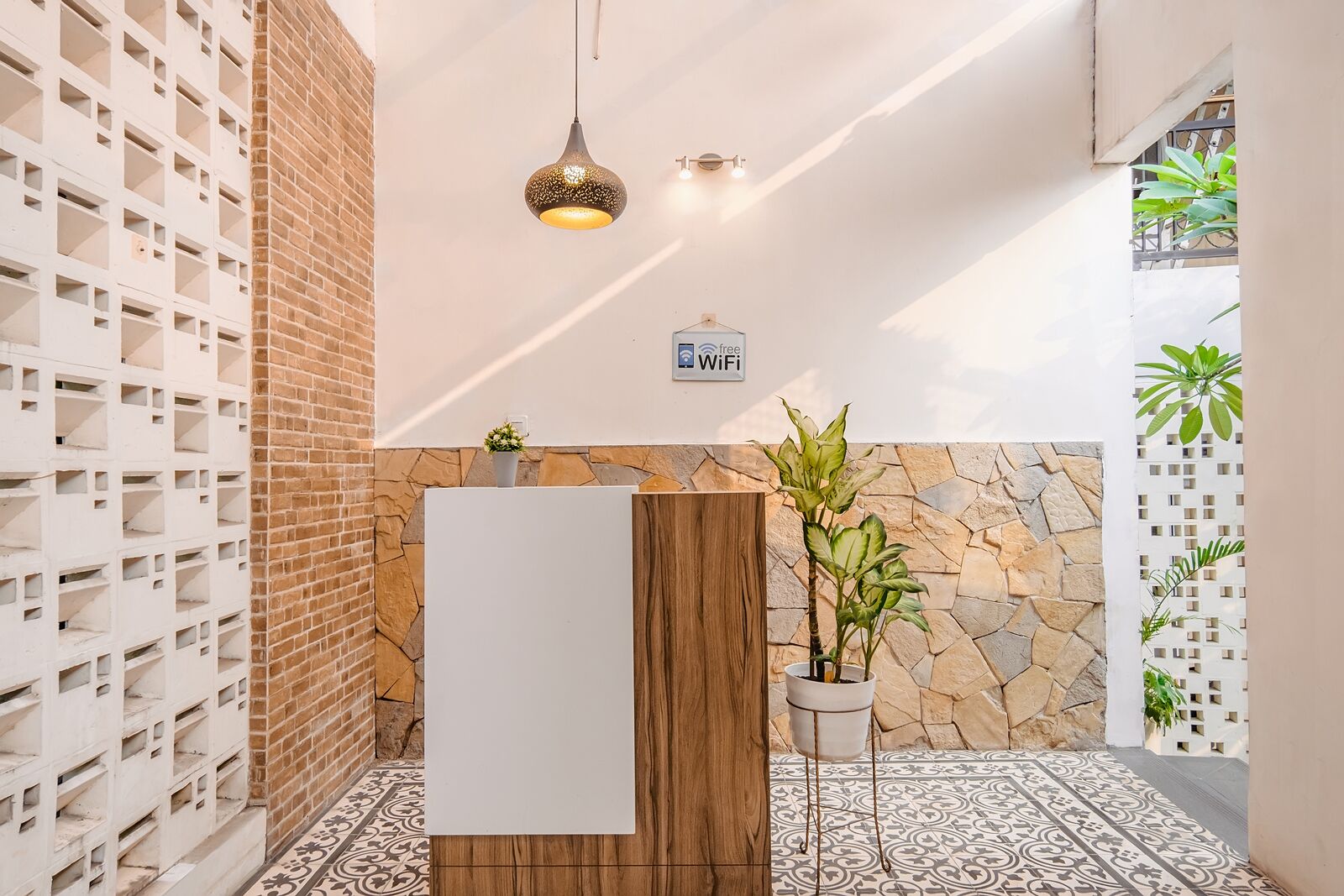 A modern bathroom with a white sink, a wooden vanity, a hanging light fixture, and a stone accent wall.
