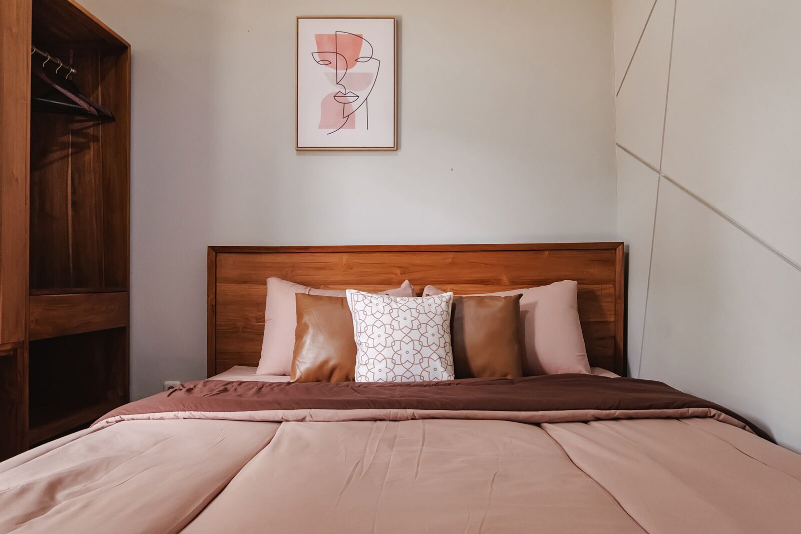 A bedroom with a wooden headboard, a bed with a brown bedspread, and a framed artwork above the bed.