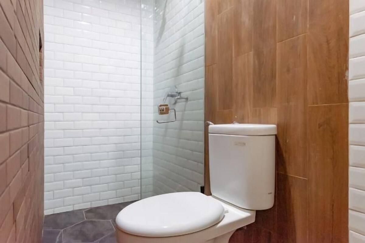 A bathroom with a white toilet, a glass shower enclosure, and a wooden wall.