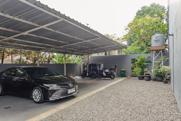 A covered parking area with a black car and a motorcycle, gravel ground, and potted plants. - Calma Coliving at Bintaro, Tangerang Selatan (South Tangerang)