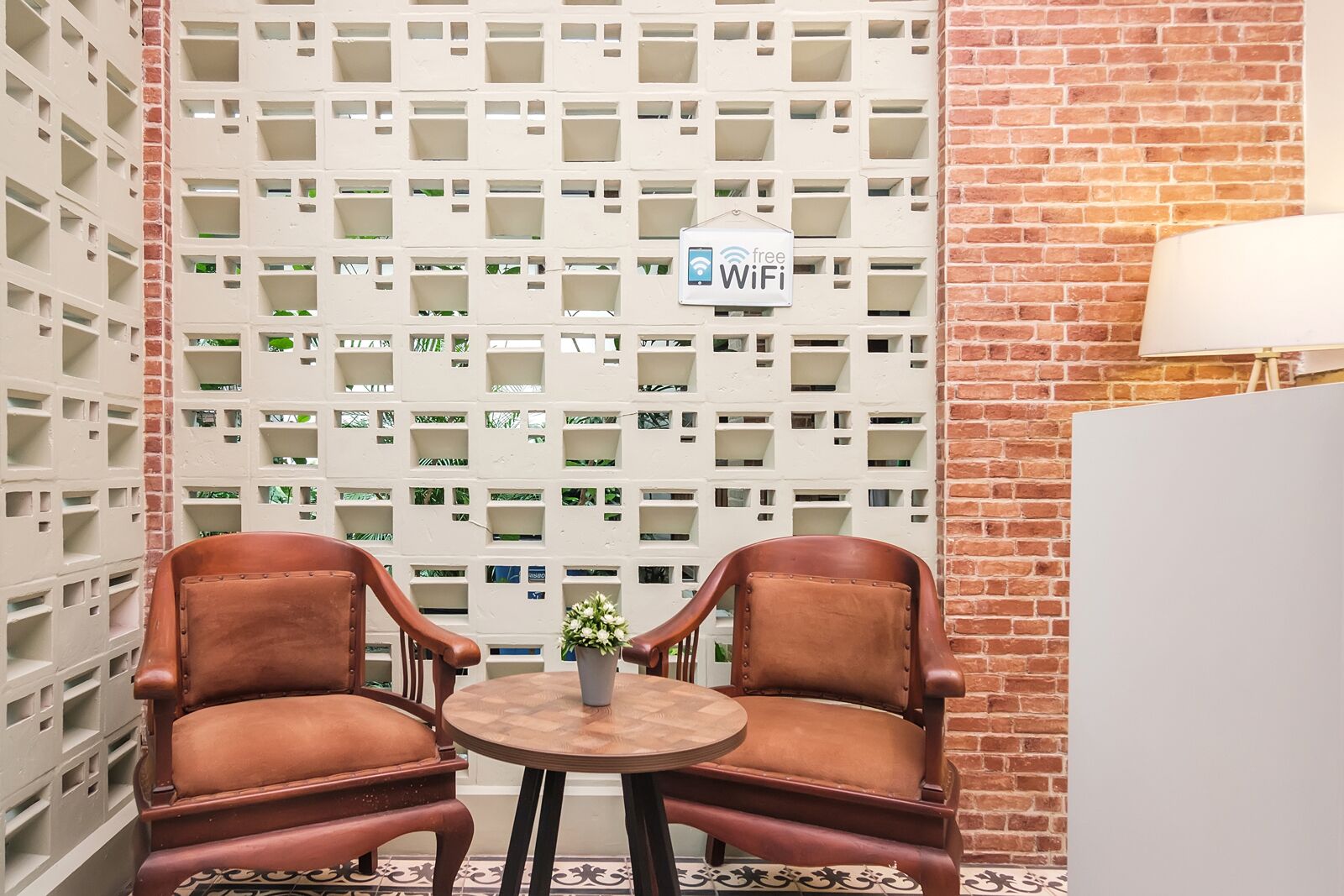 A seating area with two leather chairs and a small table, a white wall with a WiFi sign, and a brick wall.
