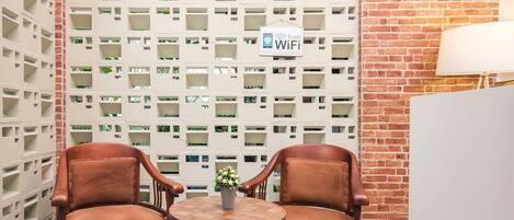 A seating area with two leather chairs and a small table, a white wall with a WiFi sign, and a brick wall.