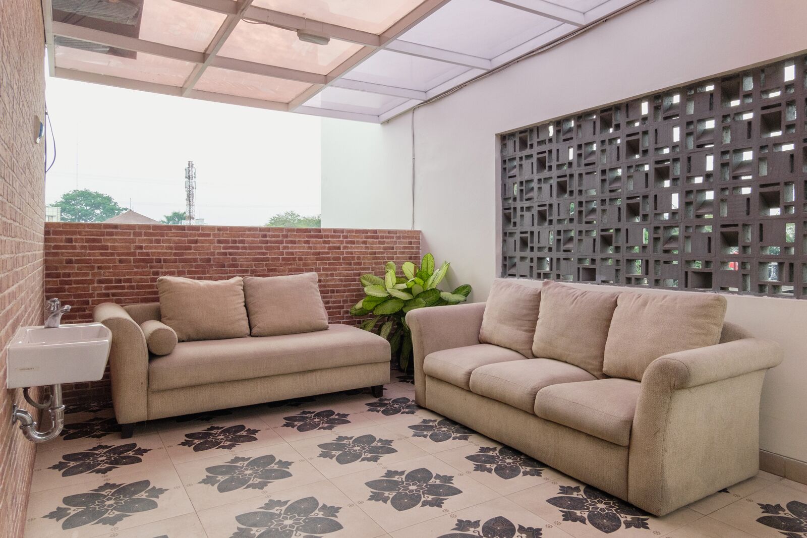 Una habitación con dos sofás color beige, una planta en maceta, un lavamanos y un panel decorativo en la pared.
