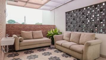 Una habitación con dos sofás color beige, una planta en maceta, un lavamanos y un panel decorativo en la pared.