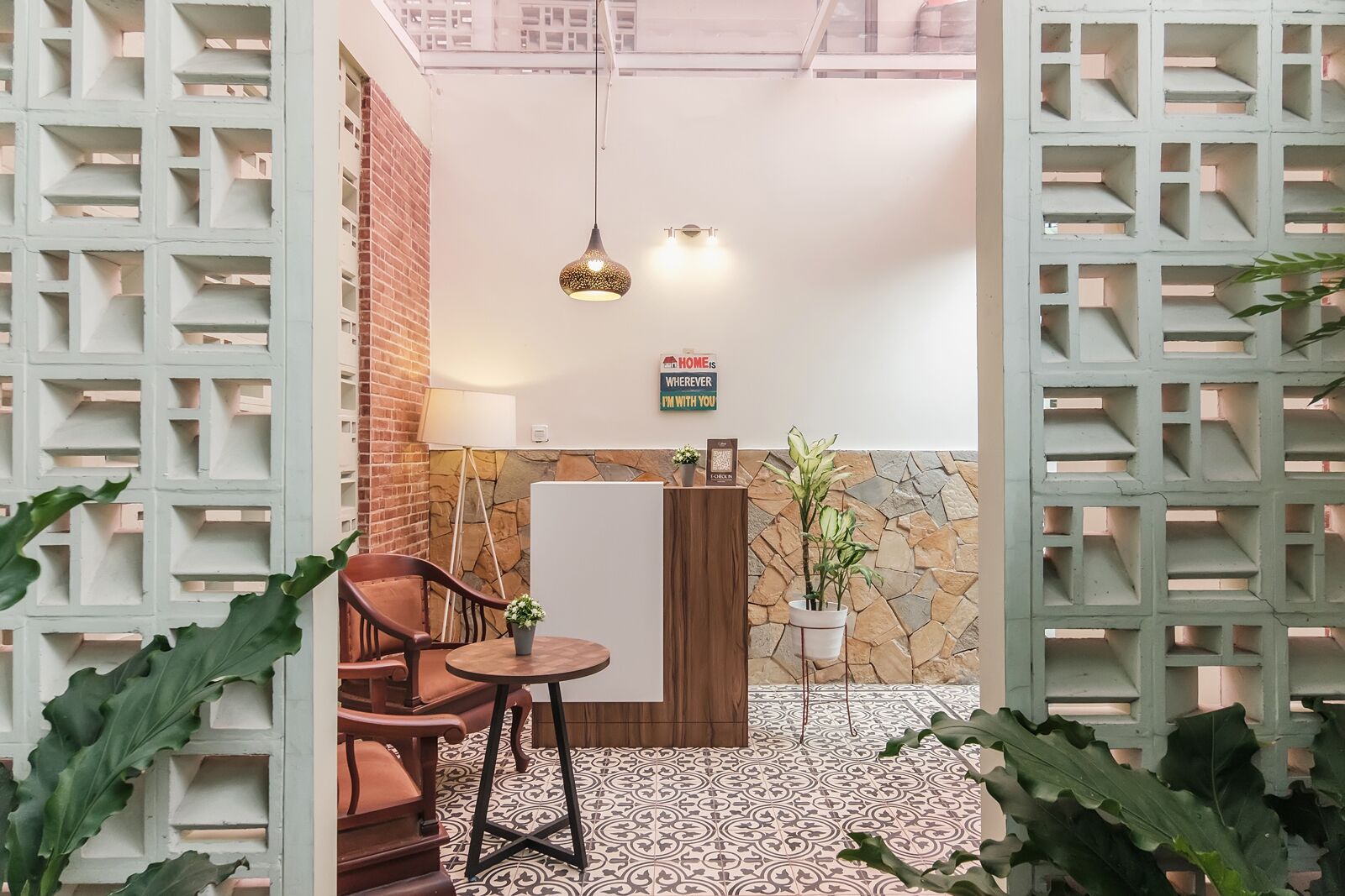 A cozy indoor space with a brick wall, a stone accent wall, a wooden cabinet, a small table with a chair, and a hanging light fixture.