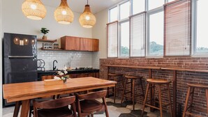 A modern kitchen with a wooden table, bar stools, and hanging light fixtures. - Calma Coliving at Bintaro, Tangerang Selatan (South Tangerang)