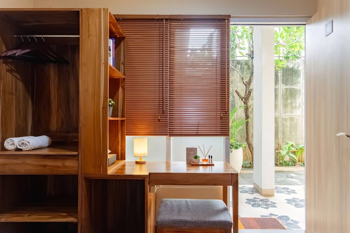 A room with a wooden desk, a lamp, a small plant, and a view of greenery outside.