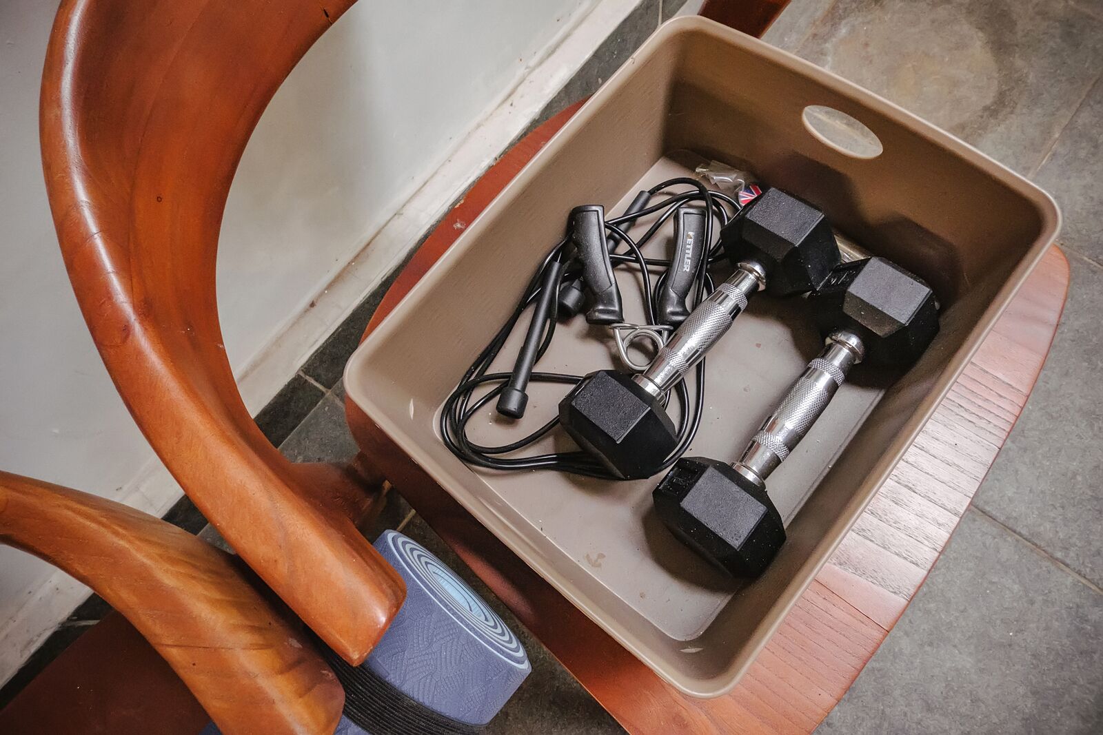 A wooden chair with a metal box containing two dumbbells and a weight plate.