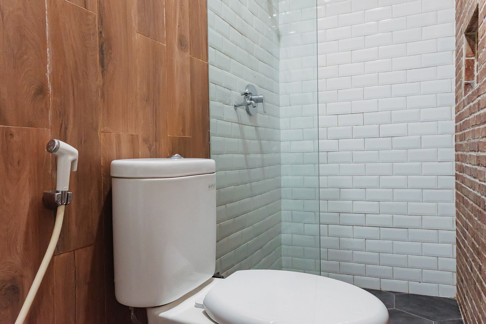 A bathroom with a white toilet, a wooden door, and a shower area with white tiled walls.