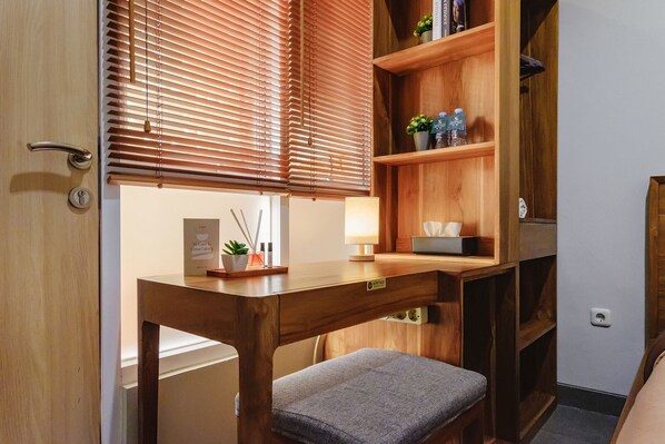 Habitación pequeña con escritorio de madera, un banco y una estantería con libros y objetos decorativos.