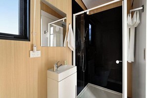 Een moderne badkamer met een douchecabine van glas, een witte wastafel en een spiegel.