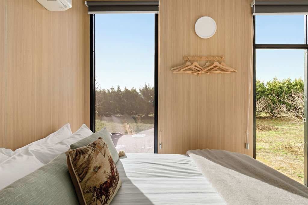A modern bedroom with a large window, a wooden wall panel, and a circular light fixture.