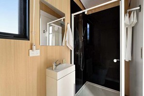 A modern bathroom with a glass shower enclosure, a white sink, and a mirror. - Tiny in the Orchard by Tiny Away (Mitchell Park)