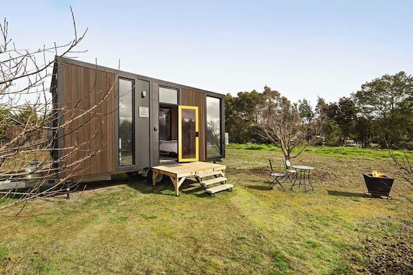 A modern, compact mobile home with a wooden deck and a small outdoor seating area. - Tiny in the Orchard by Tiny Away (Mitchell Park)