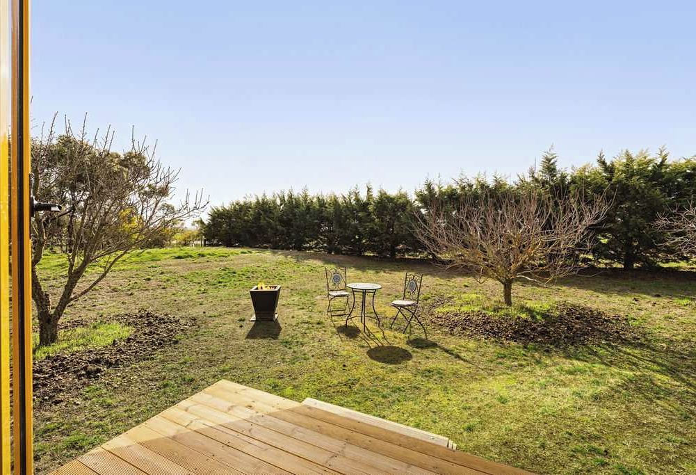 A wooden deck with a table and chairs, a fire pit, and a grassy area with trees.