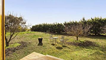 A wooden deck with a table and chairs, a fire pit, and a grassy area with trees.