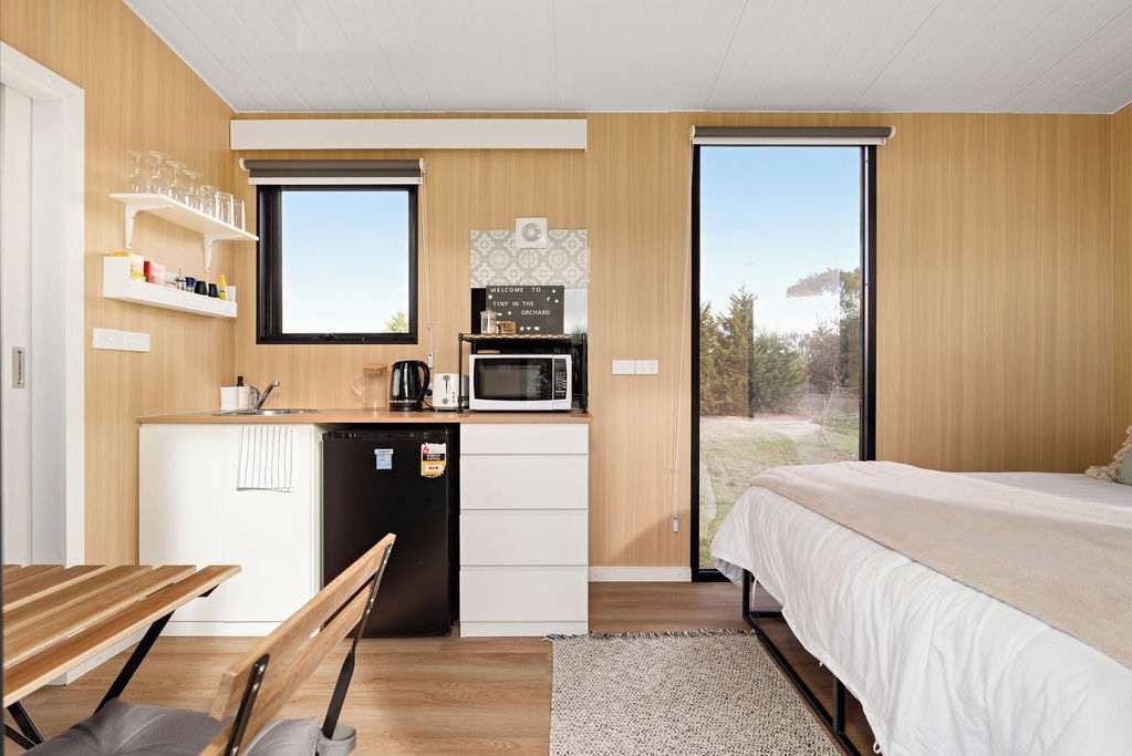 A compact room with a kitchenette, a bed, and a view through a large window.