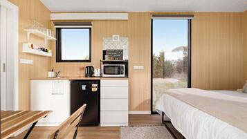 A compact room with a kitchenette, a bed, and a view through a large window.