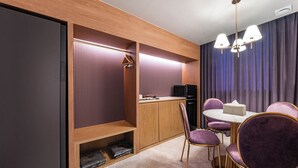 Una habitación de hotel moderna con un armario de madera, un banco empotrado, una mesa de comedor con sillas moradas y una lámpara en el techo.