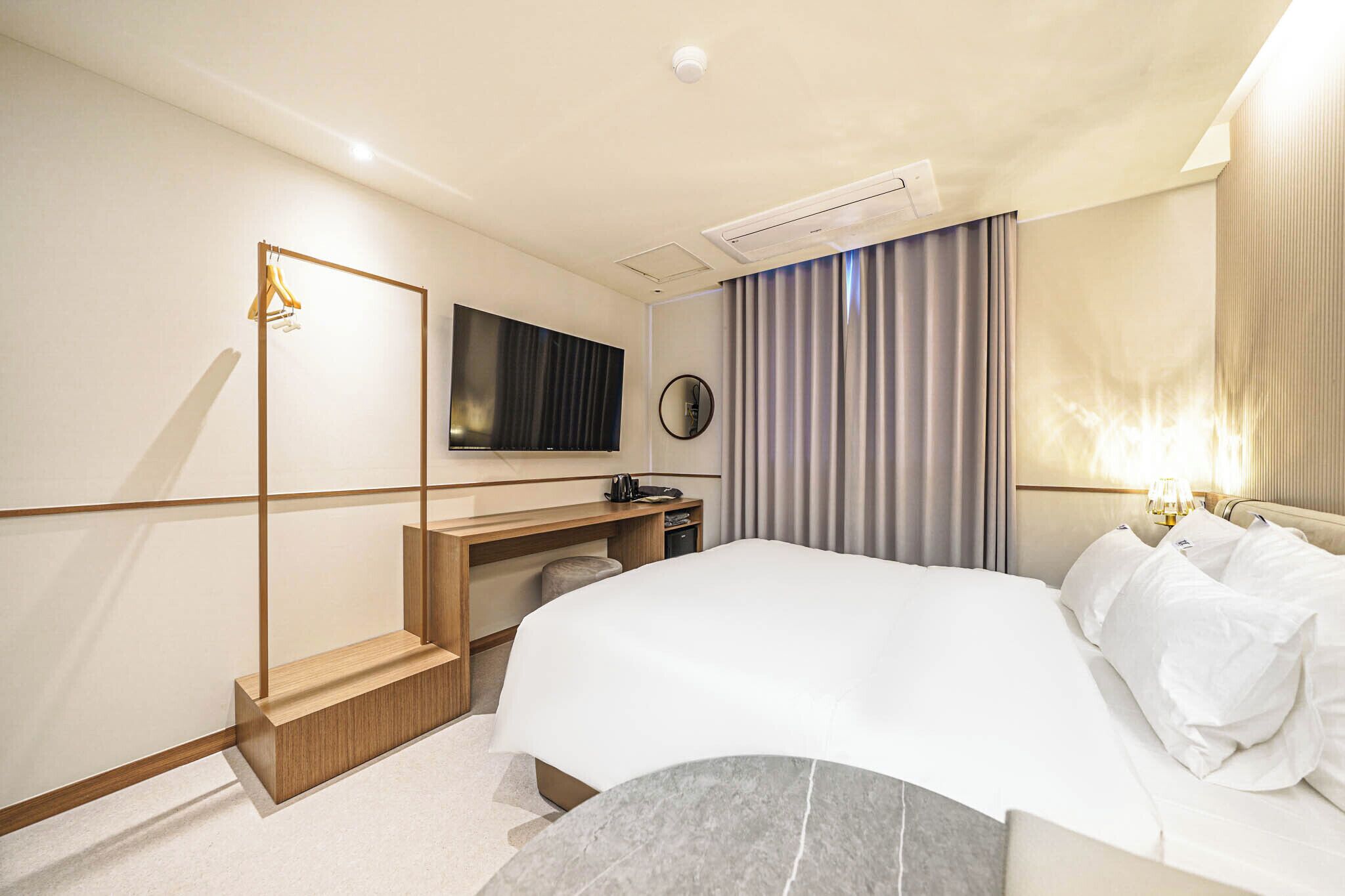 Una habitación de hotel moderna con una cama, un escritorio, un televisor de pantalla plana, un espejo y una ventana con cortinas.